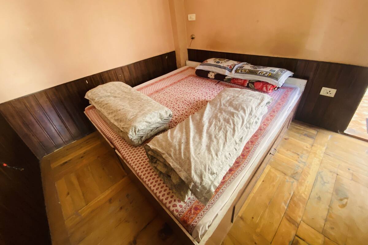 A single bed with a wooden frame, a patterned bedspread, and pillows.