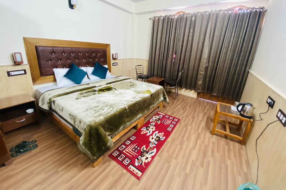 A hotel room with a wooden bed, a red decorative rug, a wooden nightstand, and a chair.