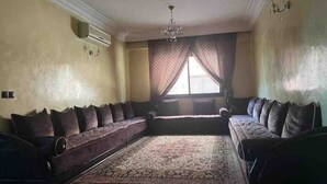 A spacious living room with a large, ornate rug, a sofa set, and a chandelier. - Superbe Appartment en Résidence Avec Piscine (Marrakech)