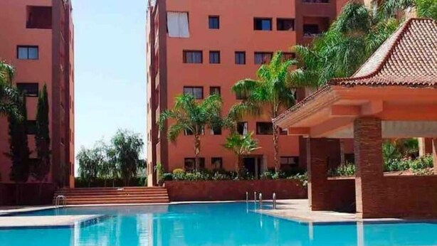 A swimming pool surrounded by a building with multiple balconies and palm trees. - Superbe Appartment en Résidence Avec Piscine (Marrakech)