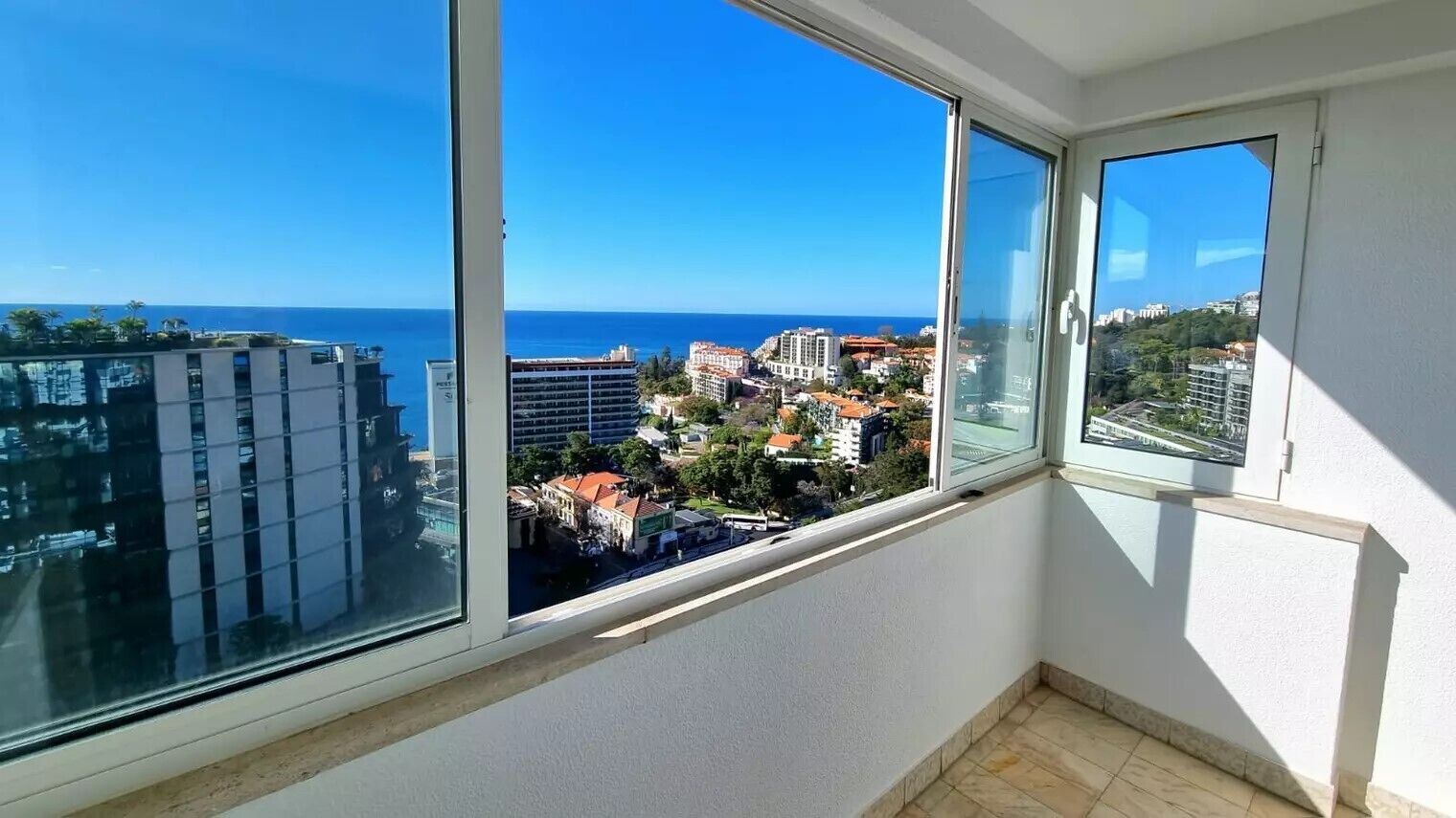 A balcony with large windows overlooking a coastal cityscape.