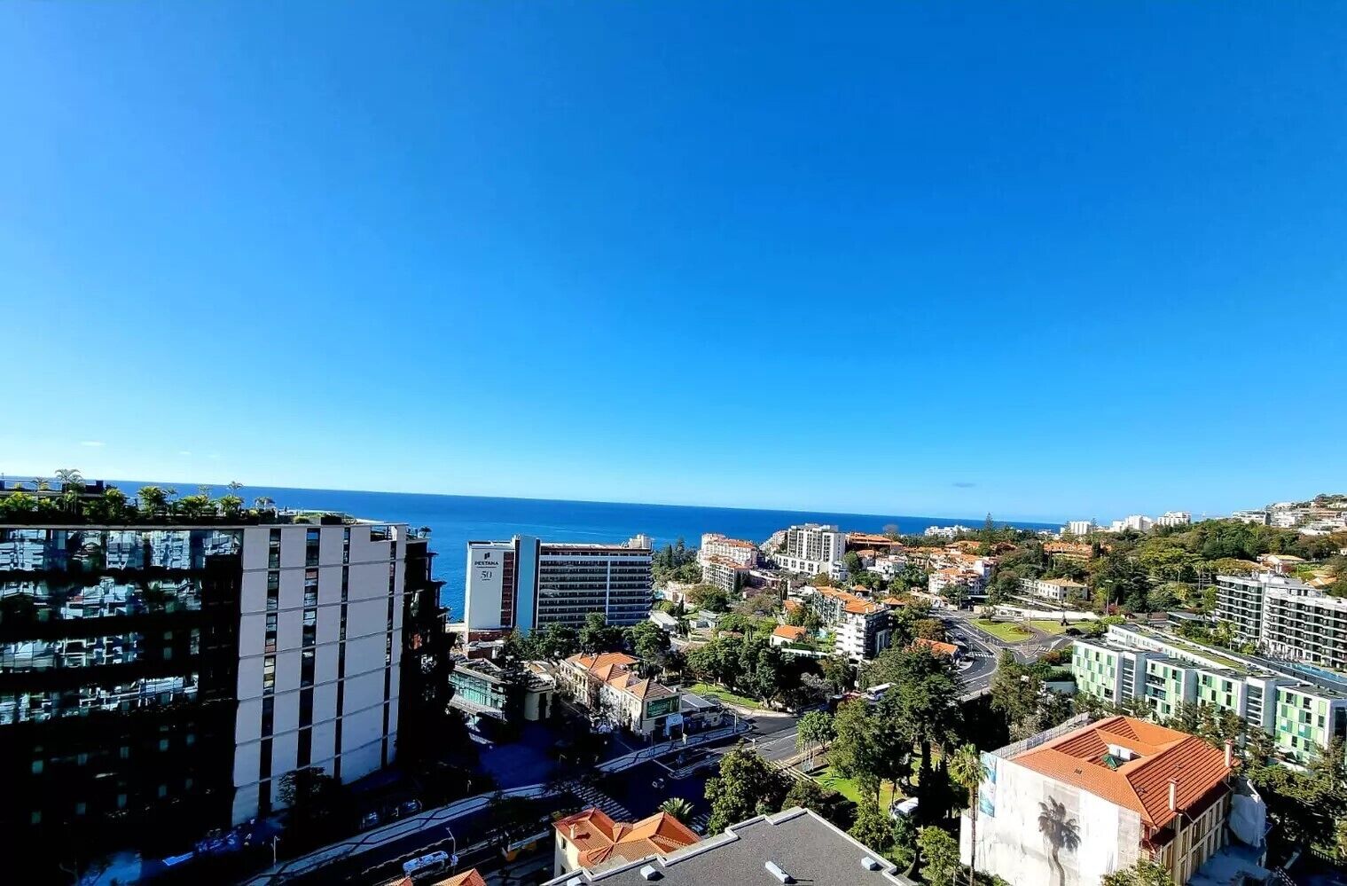 Un paysage urbain côtier avec des bâtiments modernes, un ciel bleu dégagé et une vue sur la mer.