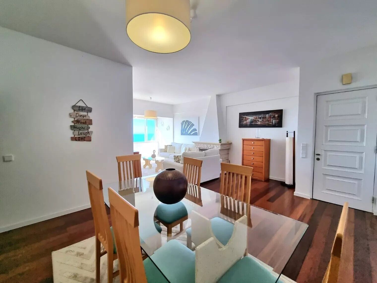 Un espace repas avec une table en verre, des chaises en bois et un vase central.