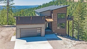 Ein modernes, zweistöckiges Haus mit Garage, Balkon und Blick auf eine bewaldete Landschaft.