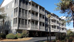 Un edificio de varios pisos con balcones, una entrada cubierta y un camino de entrada arbolado.