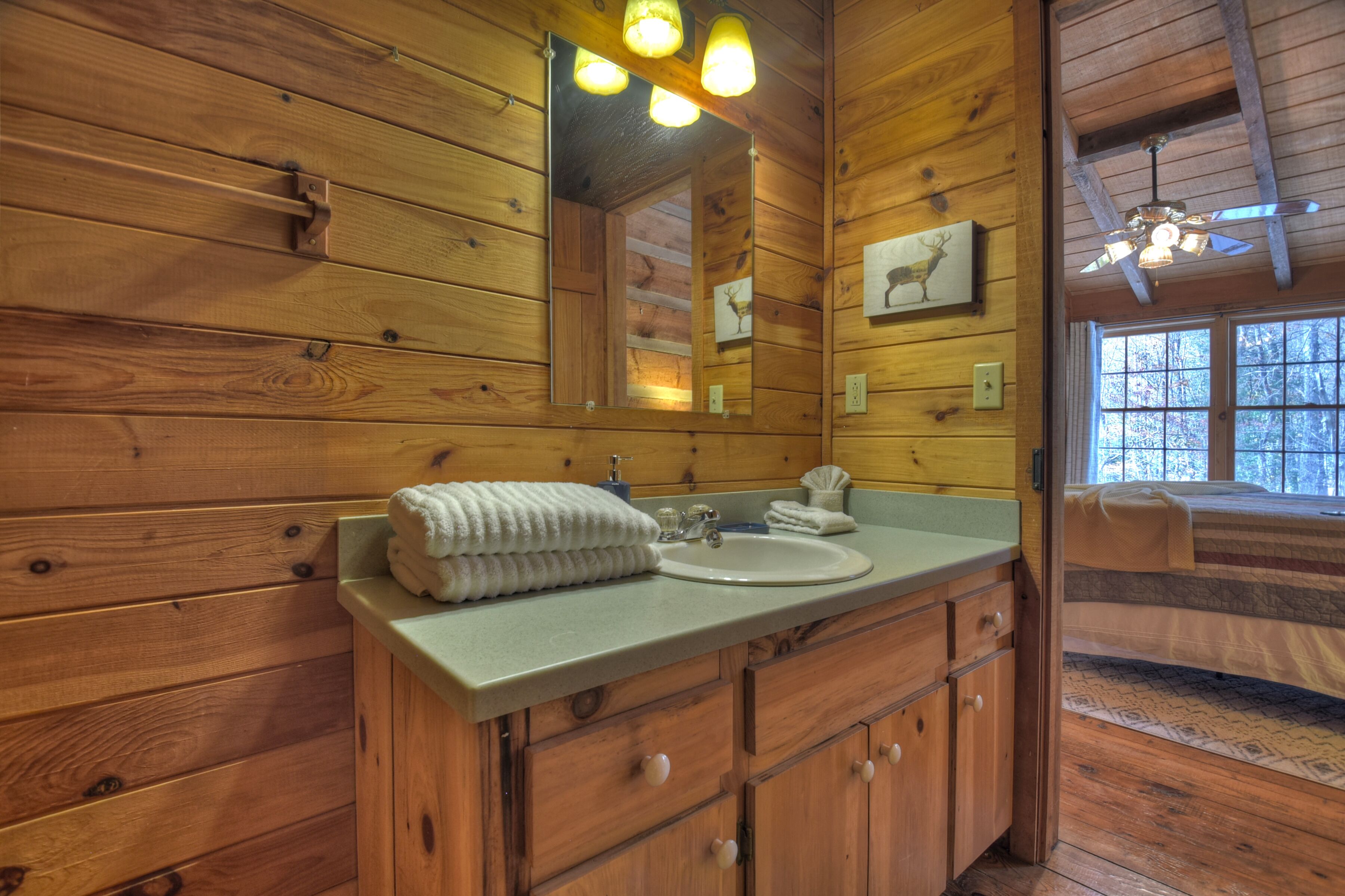 Une salle de bain rustique, aménagée dans une cabane en bois, avec un lavabo, un miroir et un lit donnant sur une fenêtre.