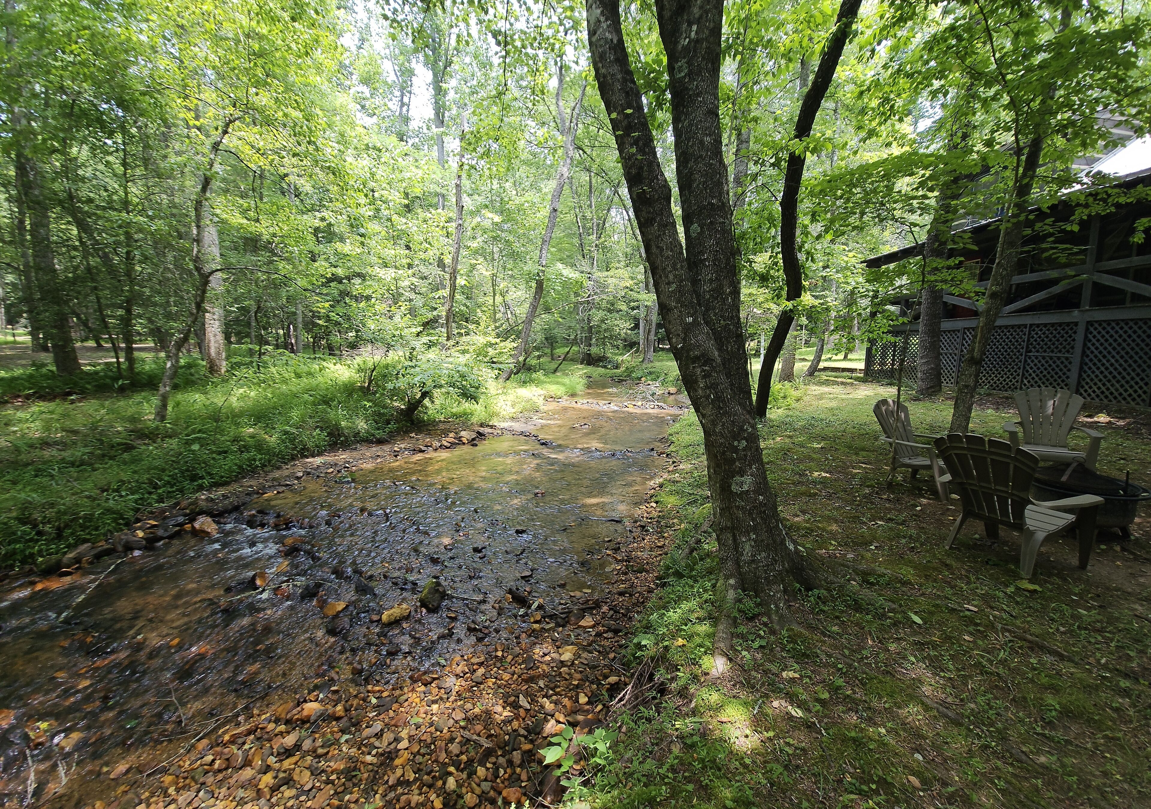 A forested area with a stream, outdoor seating, and a wooden structure.