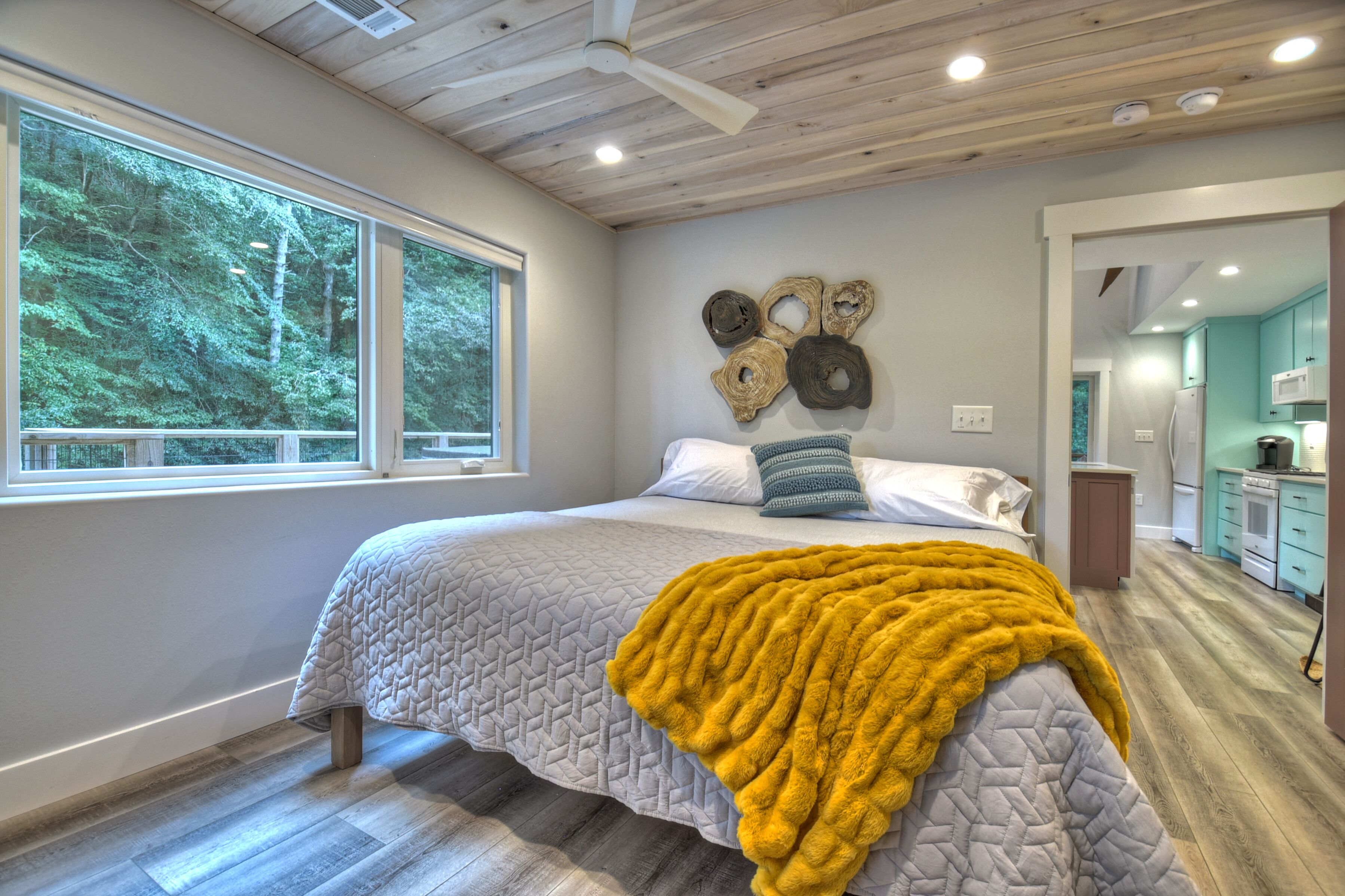 A bedroom with a bed, a large window, and a view of trees.