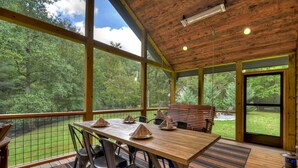 A wooden deck with a table and chairs, overlooking a grassy area with trees.