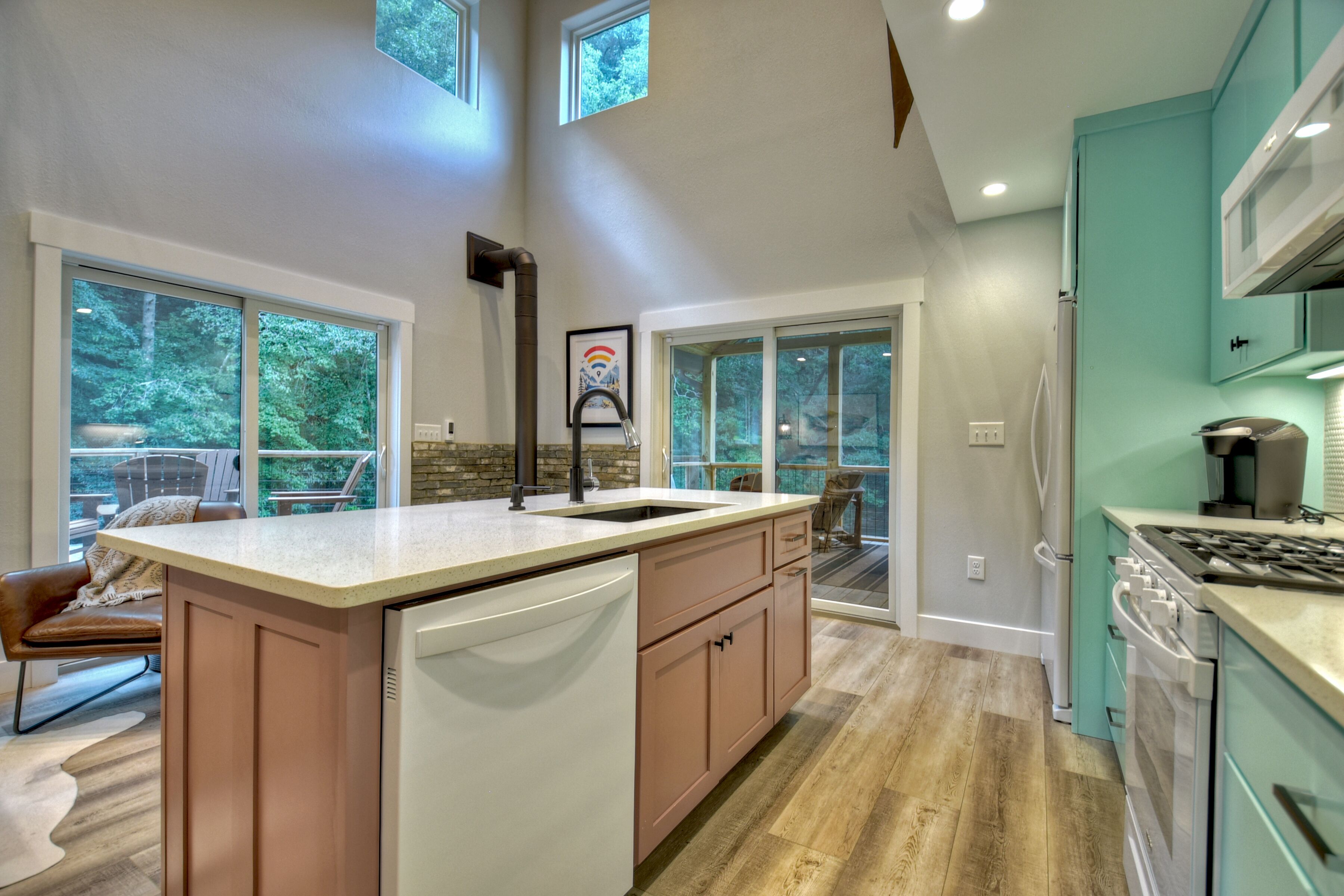 A modern kitchen with a central island, a dining area with a view, and a large window overlooking greenery.