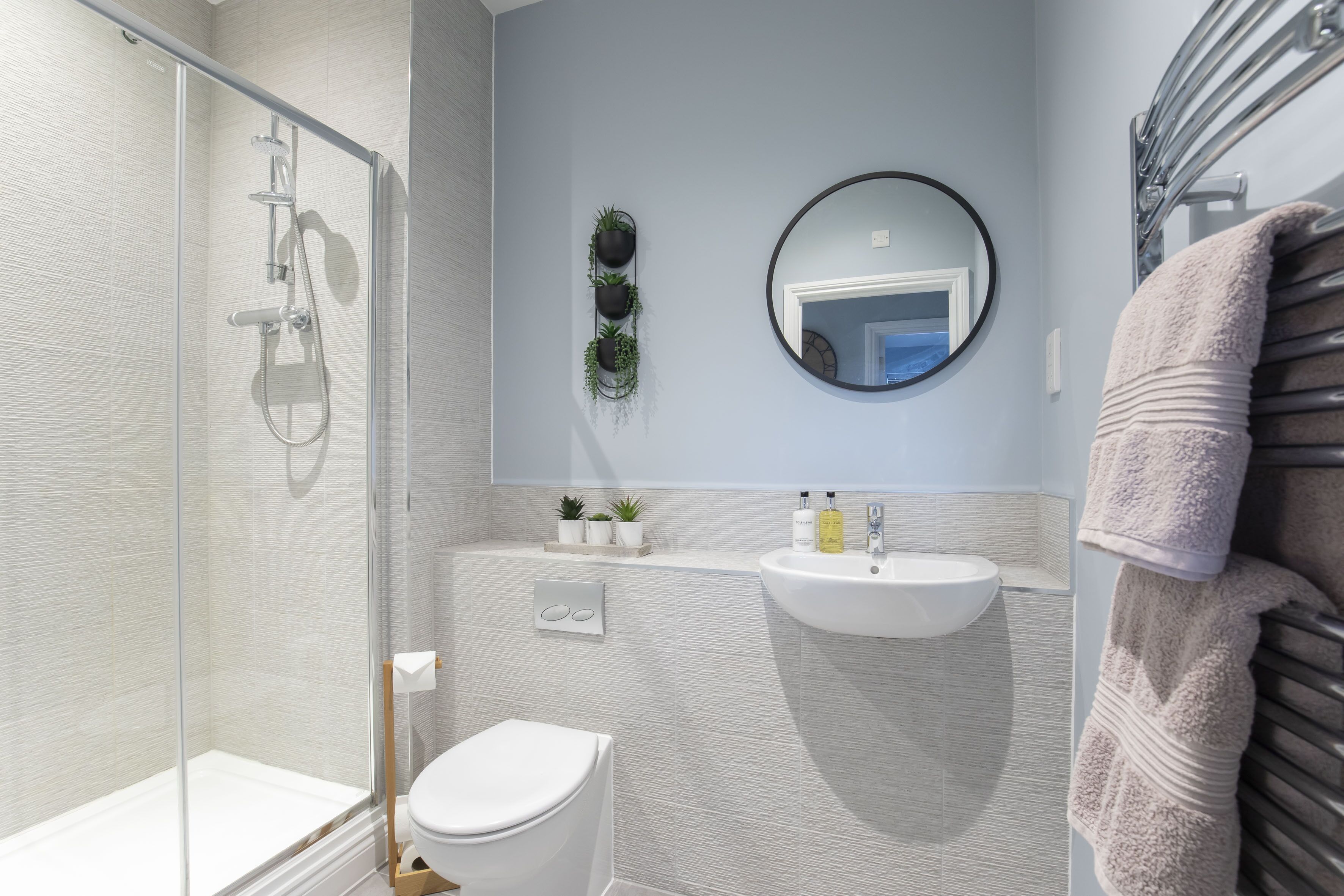 A modern bathroom with a glass shower enclosure, a white toilet, a sink with a mirror above, and a towel rack with a towel.
