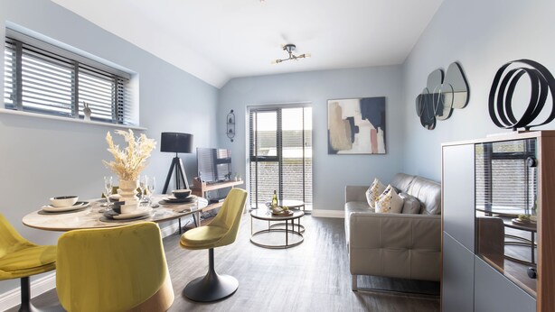 A modern living room with a dining area, featuring a sofa, chairs, a coffee table, and artwork on the walls. - Elliot Oliver - Luxurious Two Bedroom Apartment in The Docks (Gloucester)