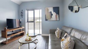 A modern living room with a sofa, coffee table, TV, and artwork on the wall. - Elliot Oliver - Luxurious Two Bedroom Apartment in The Docks (Gloucester)
