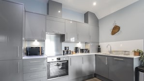 A modern kitchen with grey cabinets, a built-in oven, and a microwave. - Elliot Oliver - Luxurious Two Bedroom Apartment in The Docks (Gloucester)