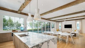 A modern kitchen with a marble island, wooden beams, and large windows. - STEPS to Private Beach! Private Pool, Game Room, 6 Bikes! Brand New, Sleeps 20! (Rosemary Beach)