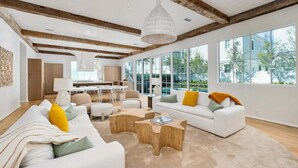 A modern living room with white sofas, wooden coffee tables, and large windows offering a view of the outdoors. - STEPS to Private Beach! Private Pool, Game Room, 6 Bikes! Brand New, Sleeps 20! (Rosemary Beach)