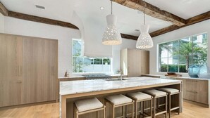 A modern kitchen with a large island, wooden bar stools, and pendant lighting. - STEPS to Private Beach! Private Pool, Game Room, 6 Bikes! Brand New, Sleeps 20! (Rosemary Beach)