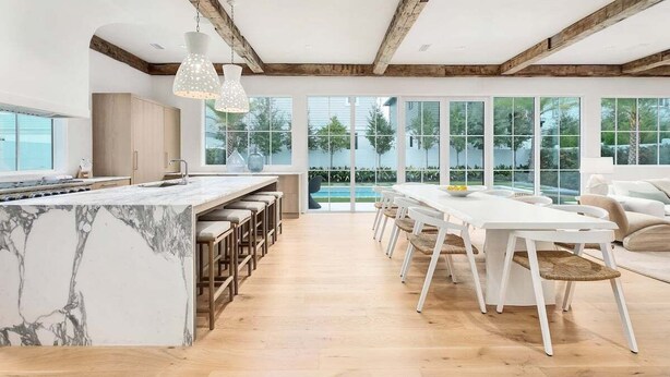 A modern kitchen with a marble island, wooden bar stools, and a large dining table with white chairs. - STEPS to Private Beach! Private Pool, Game Room, 6 Bikes! Brand New, Sleeps 20! (Rosemary Beach)