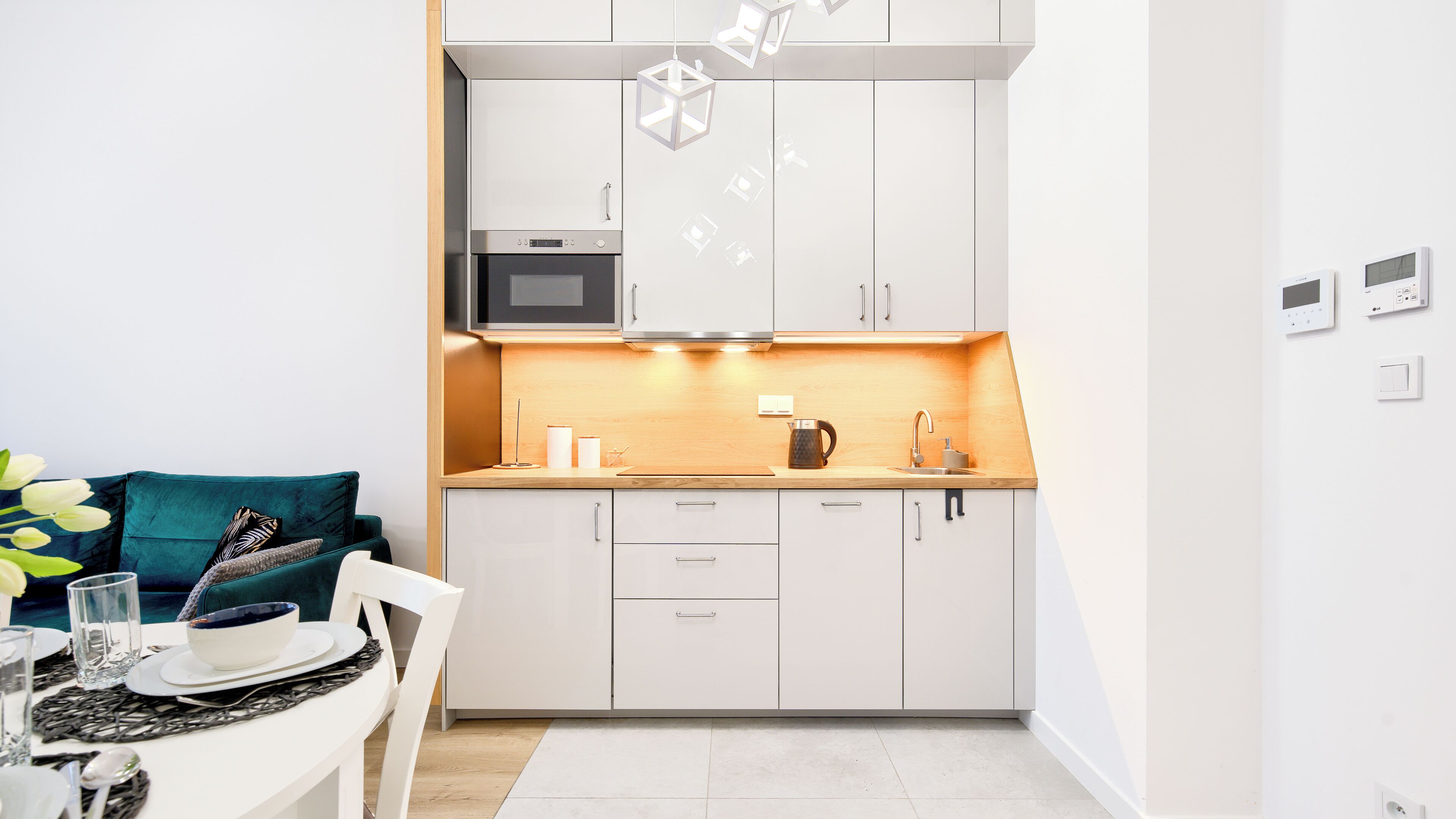 Una cocina moderna con armarios blancos, microondas, hervidor y comedor con una mesa dispuesta para dos.
