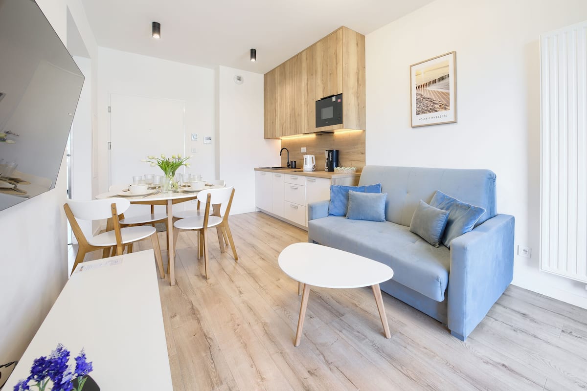 A modern living space with a dining area, a kitchenette, a blue sofa, and a white coffee table.