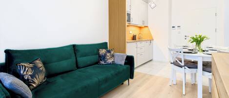 Una sala de estar moderna con un sofá verde, una mesa de comedor con sillas y una zona de cocina al fondo.