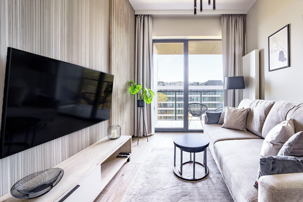 A modern living room with a large flat-screen TV, a sofa, a coffee table, and a potted plant.