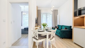 A modern living space with a dining area, a green sofa, and a TV mounted on the wall. - Apartamenty Sun & Snow Shellter (Trzebiatow)