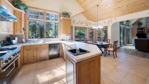 A spacious kitchen with wooden cabinets, a large island, and a dining area with a table and chairs. - Wishram Retreat - 24 Wishram Trail (Graeagle)