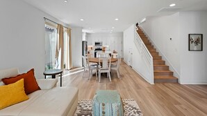 A modern living room with a sofa, coffee table, and a staircase leading to a kitchen area. - Desert home w/ BBQ, fire pit & pool (La Quinta)