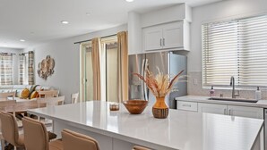 A modern kitchen with a central island, white cabinetry, and a stainless steel refrigerator. - Desert home w/ BBQ, fire pit & pool (La Quinta)