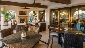 A spacious outdoor patio with wicker furniture, a glass table, and a fireplace. - Desert home w/ BBQ, fire pit & pool (La Quinta)