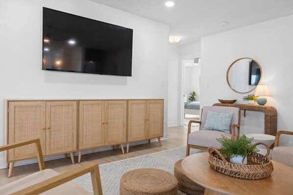 A modern living room with a flat-screen TV, wicker furniture, and a rattan cabinet.