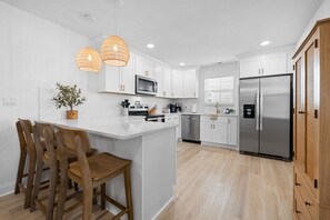 Una cocina moderna con armarios blancos, una isla central con sillas, un refrigerador de acero inoxidable y un microondas.