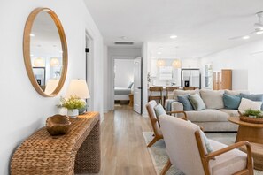 Una sala de estar moderna con un sofá, sillas, una mesa de centro, una lámpara, un espejo y una consola decorada con objetos decorativos.