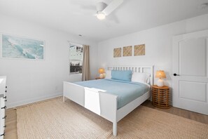 A bedroom with a white bed, a window with curtains, a white radiator, and two bedside lamps.