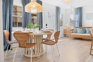 Ein modernes Wohnzimmer mit einem runden Esstisch, Korbstühlen, einem Holzsofa und einer hängenden Leuchte.