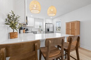 Una cocina moderna con armarios blancos, una isla central y dos lámparas colgantes.