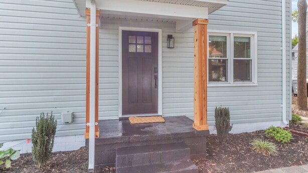 Una casa con puerta principal oscura, un pequeño porche de madera y un buzón.