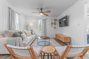 Ein modernes Wohnzimmer mit einer Couch, zwei Sesseln, einem Couchtisch, einem Fernseher und einem Deckenventilator.