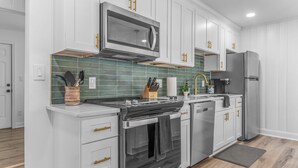 Una cocina moderna con armarios blancos, un microondas de acero inoxidable, un horno empotrado y un refrigerador.