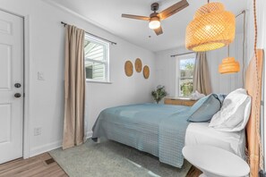A bedroom with a bed, a ceiling fan, a window with curtains, and a small table. - The Comber Renovated 2023 2bd Luxury House 2 blocks from beach (Virginia Beach)