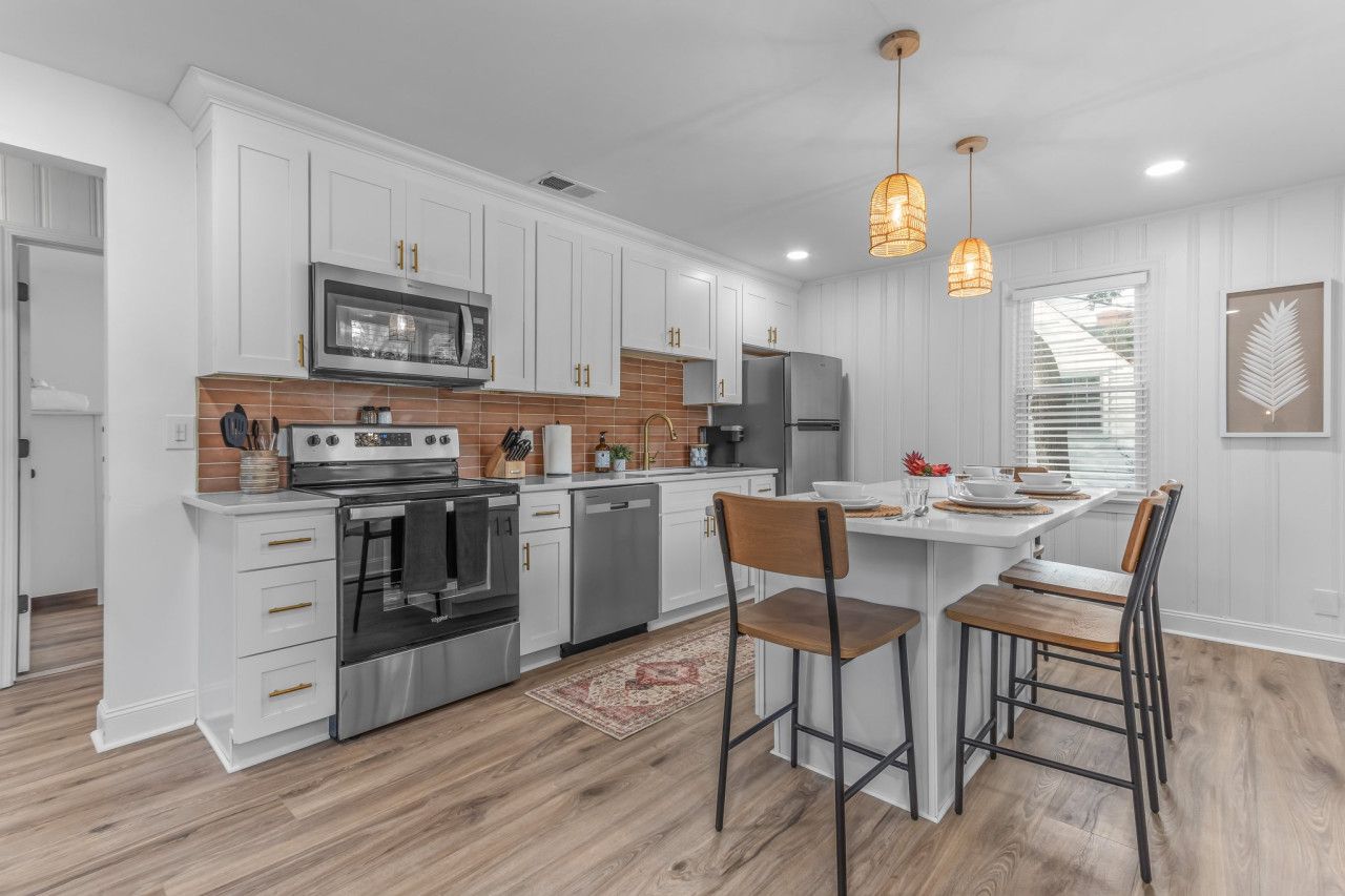 A modern kitchen with white cabinetry, stainless steel appliances, and a central island with bar stools.