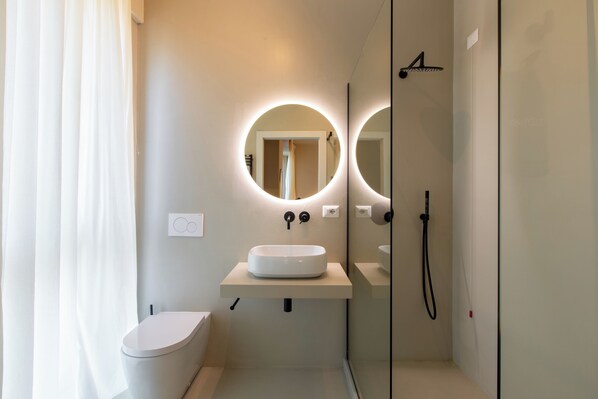 A modern bathroom with a toilet, a sink with a mirror, and a shower. - Daplace - Corso Sempione Suites (Milan)