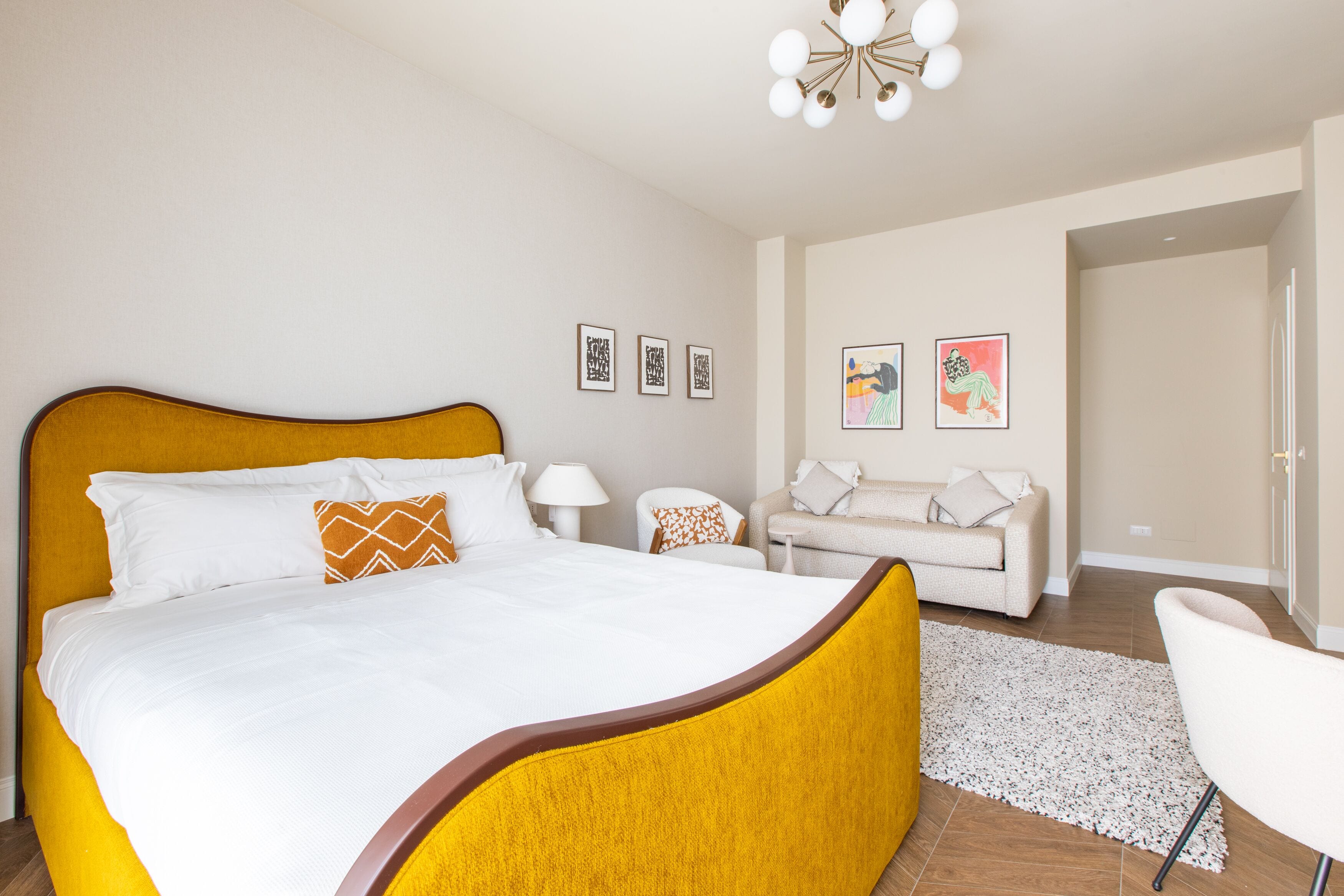 A hotel room with a large bed, a sofa, a chair, and artwork on the walls.