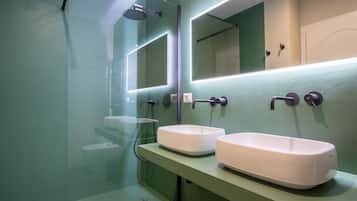 Un baño moderno con dos lavamanos blancos, cabina de ducha con paredes de vidrio e iluminación integrada en el espejo.