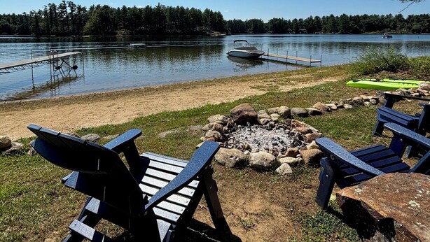 Eine Seenlandschaft mit Adirondack-Stühlen, einem Steg und einem Boot.
