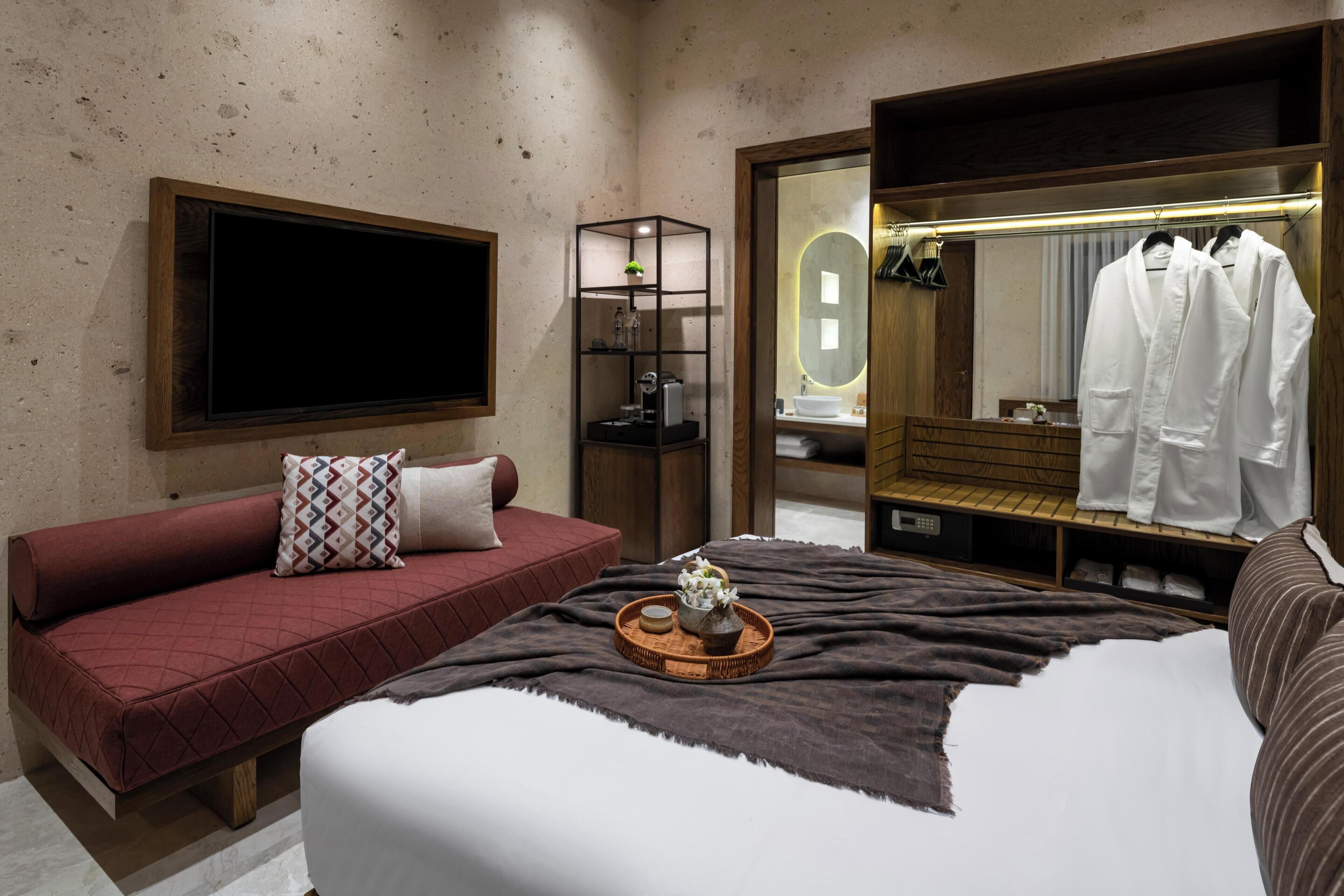 Een hotelkamer met een groot bed, een rode bank, een houten bijzettafeltje, een spiegel en een kledingkast.