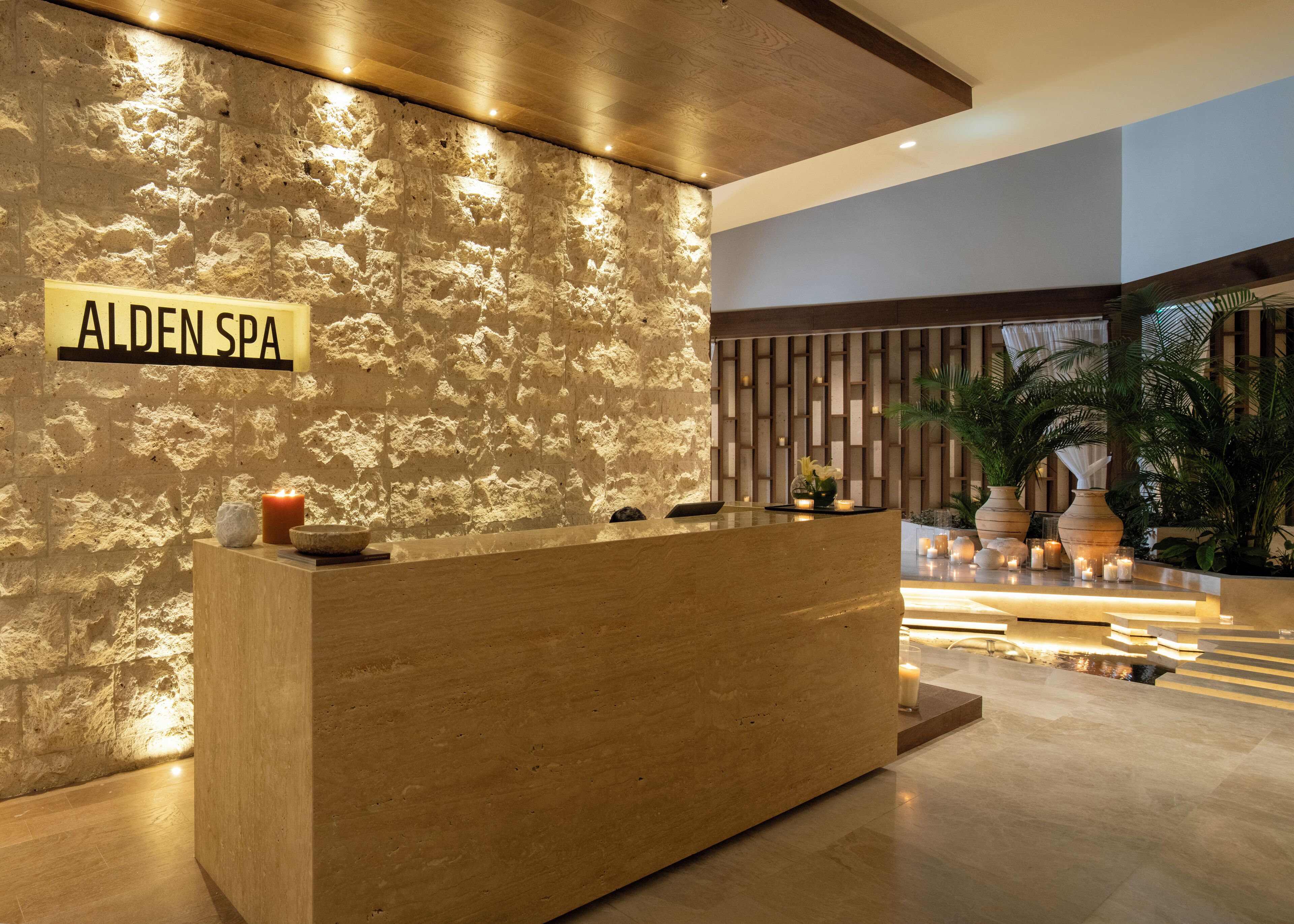 A reception desk with a stone wall backdrop and a sign reading "ALDEN SPA".