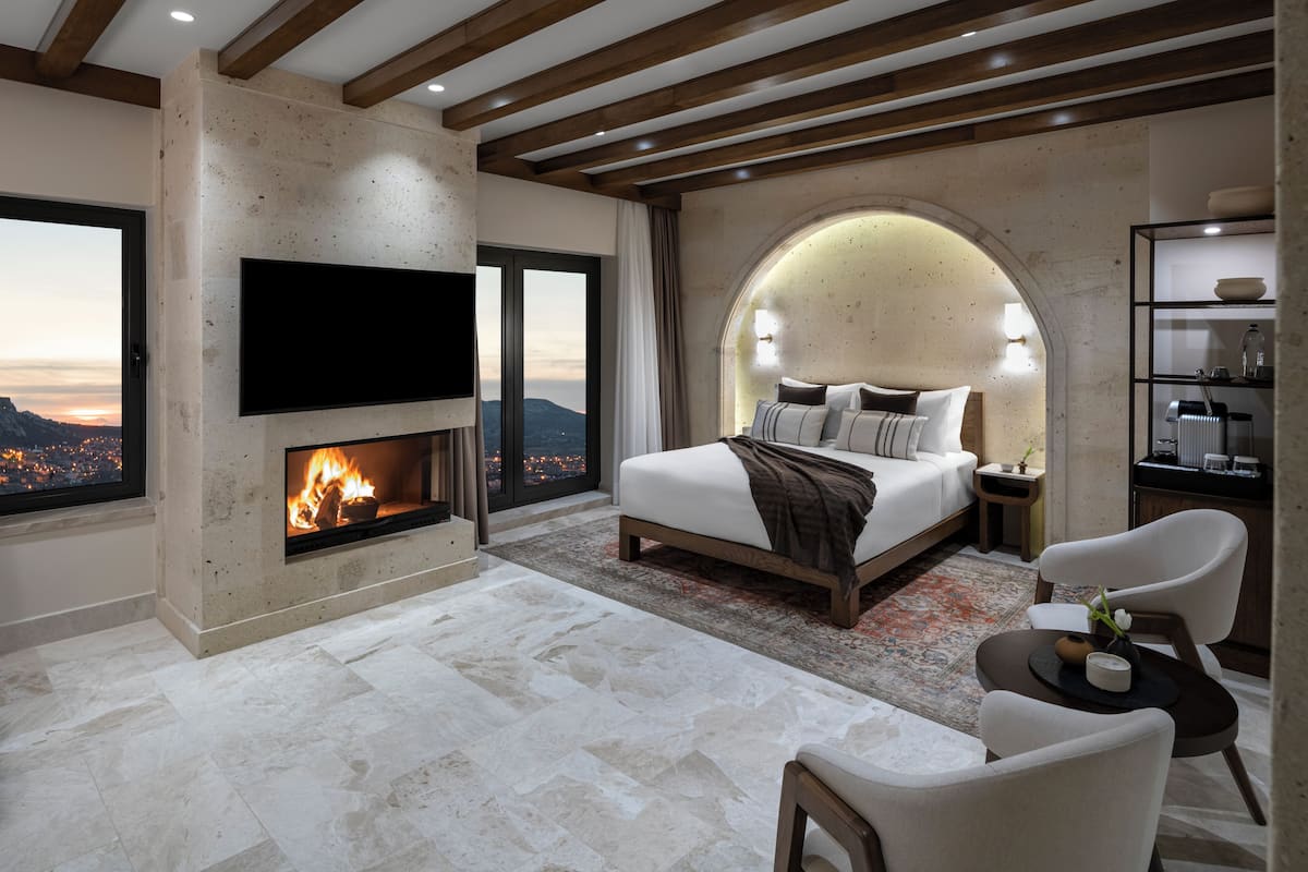 Un dormitorio con chimenea, una cama grande, un televisor y vistas de la ciudad.