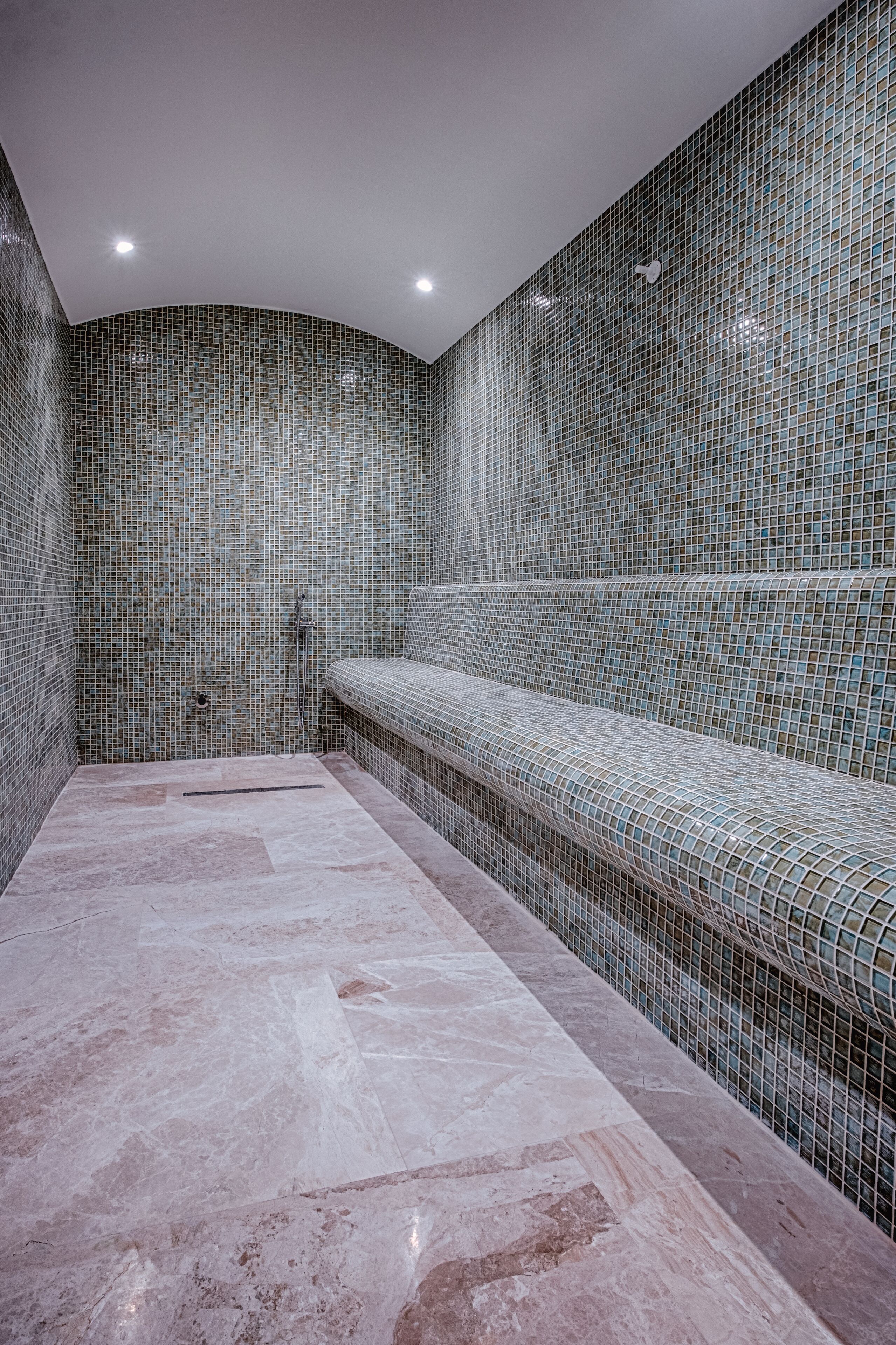 Ein Spa-Raum mit einer gefliesten Wand, einer Sitzbank und einem Marmorboden.